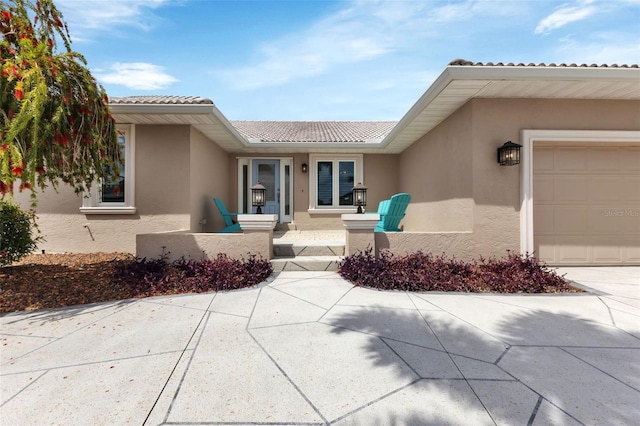 property entrance featuring stucco siding, an attached garage, and a tile roof