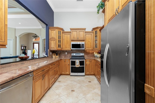 kitchen with ornamental molding, decorative columns, stainless steel appliances, and tasteful backsplash