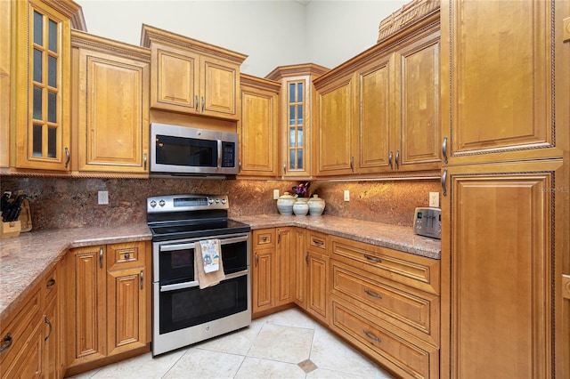 kitchen with light tile patterned flooring, brown cabinets, appliances with stainless steel finishes, and decorative backsplash