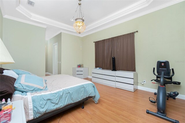 bedroom with ornamental molding, visible vents, a raised ceiling, and light wood-style floors