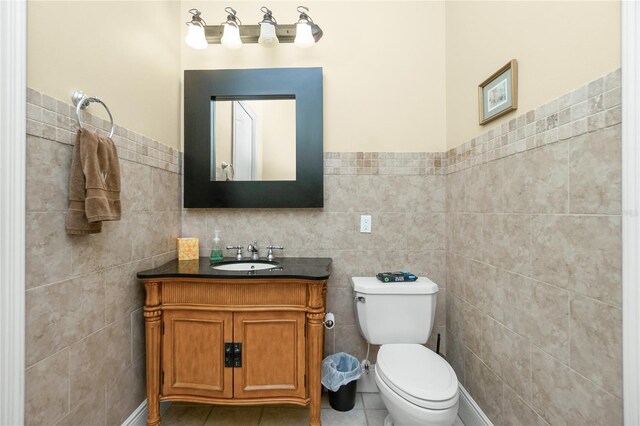 half bath featuring tile patterned floors, tile walls, a wainscoted wall, toilet, and vanity