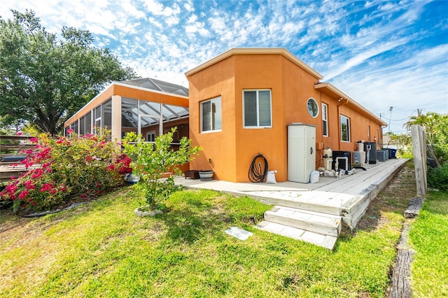 rear view of property with a patio area, glass enclosure, central air condition unit, stucco siding, and a yard