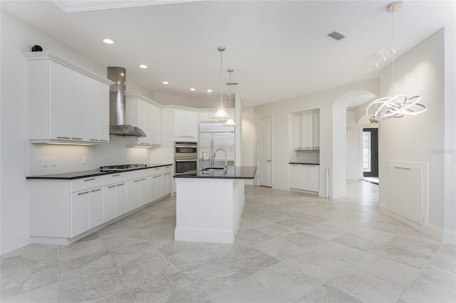 kitchen featuring tasteful backsplash, wall chimney range hood, dark countertops, appliances with stainless steel finishes, and arched walkways