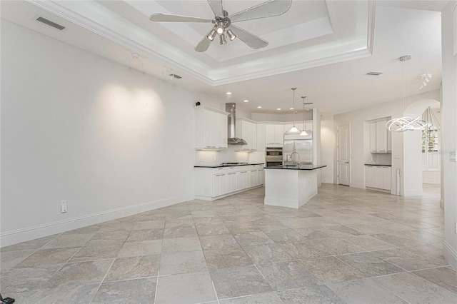 kitchen with wall chimney range hood, baseboards, dark countertops, and a raised ceiling