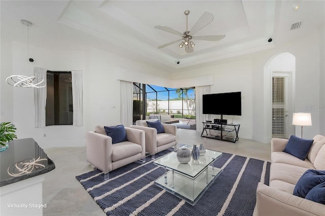 living room with crown molding, arched walkways, a ceiling fan, visible vents, and a raised ceiling