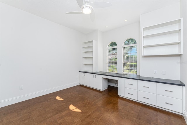unfurnished office featuring built in features, ceiling fan, dark wood-style flooring, built in study area, and baseboards