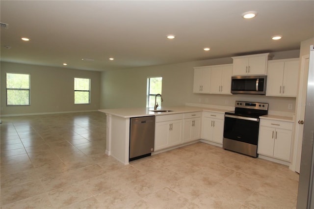 kitchen with open floor plan, a peninsula, white cabinetry, appliances with stainless steel finishes, and a sink