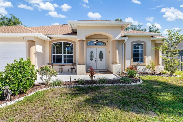 16450 Bauers Ave, Port Charlotte, FL 33954 - view of exterior entry with a lawn, a shingled roof, stucco siding, and an attached garage