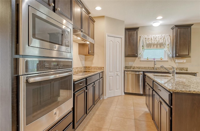 kitchen with dark brown cabinets, appliances with stainless steel finishes, light stone counters, under cabinet range hood, and light tile patterned floors