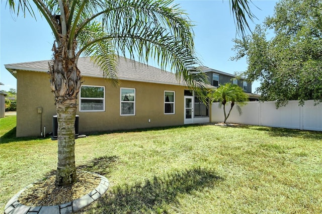 back of property with central AC, fence, a shingled roof, a yard, and stucco siding
