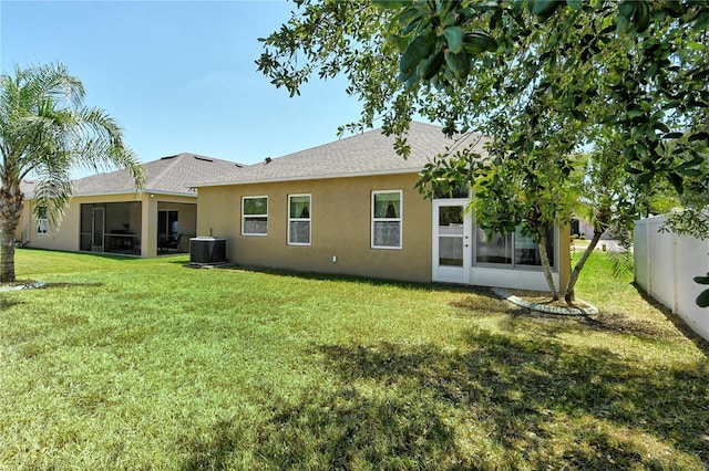 rear view of property featuring a shingled roof, a sunroom, a yard, and stucco siding