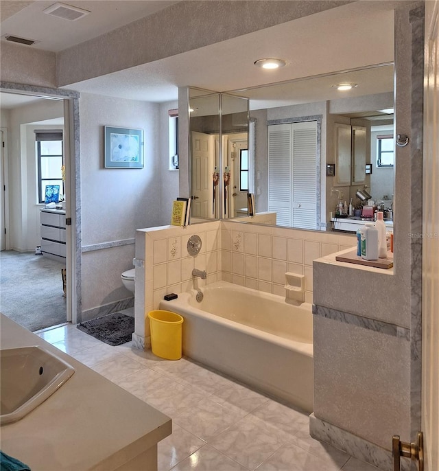 bathroom featuring plenty of natural light, a garden tub, visible vents, vanity, and toilet