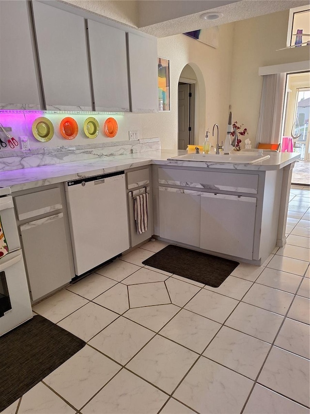 kitchen featuring white dishwasher, a sink, light countertops, arched walkways, and a peninsula