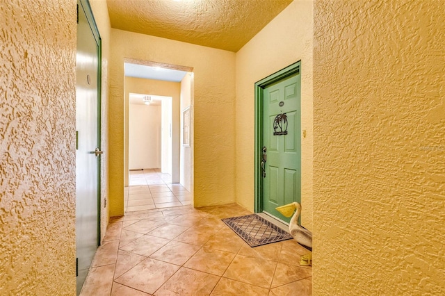 hallway featuring a textured ceiling, a textured wall, and light tile patterned flooring