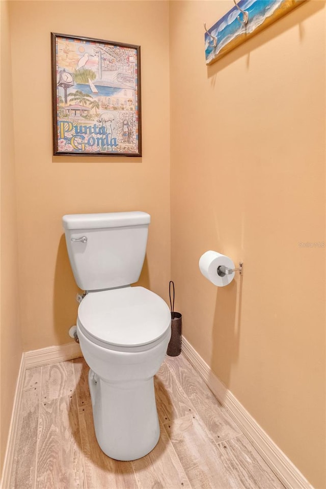 bathroom with toilet, baseboards, and wood finished floors