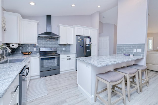 kitchen with wall chimney exhaust hood, light wood-style flooring, a sink, vaulted ceiling, and appliances with stainless steel finishes
