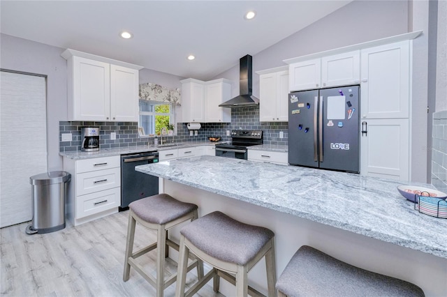 kitchen featuring wall chimney exhaust hood, a sink, white cabinetry, a breakfast bar, and appliances with stainless steel finishes