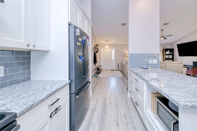 kitchen with light stone countertops, appliances with stainless steel finishes, white cabinets, backsplash, and open floor plan
