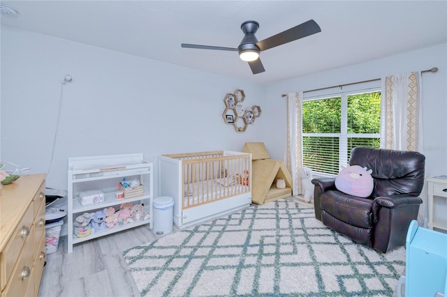 bedroom featuring a crib, a ceiling fan, and wood finished floors