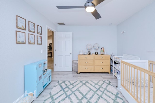 bedroom featuring light wood-style floors, visible vents, a ceiling fan, and a nursery area