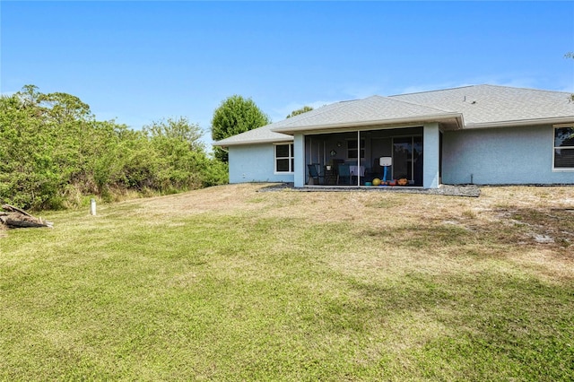 rear view of house featuring stucco siding, a sunroom, and a yard