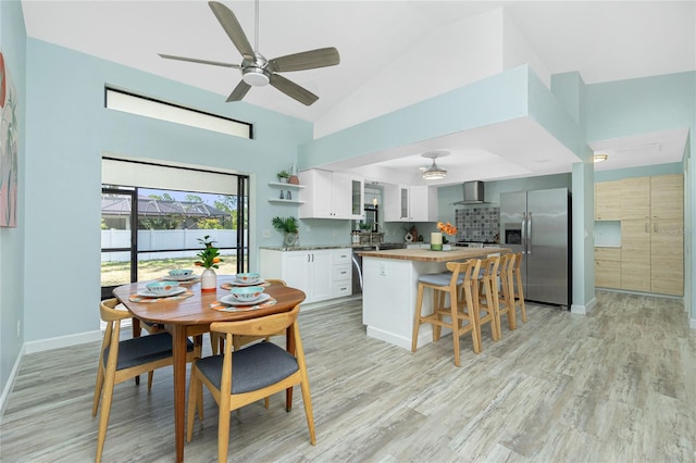 dining room featuring light wood-style flooring, high vaulted ceiling, baseboards, and a ceiling fan