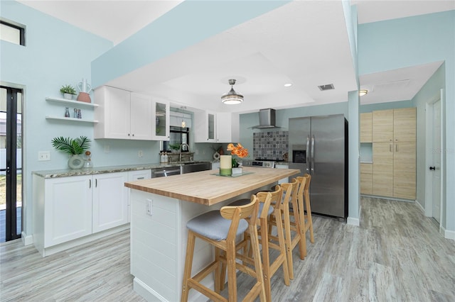 kitchen featuring stainless steel appliances, wood counters, wall chimney exhaust hood, and light wood finished floors