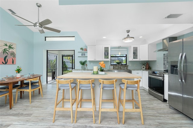 kitchen with white cabinetry, wall chimney range hood, appliances with stainless steel finishes, and visible vents