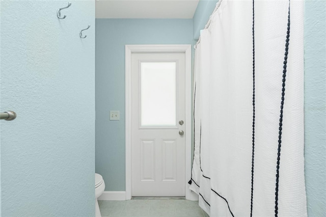 full bath with toilet, tile patterned floors, a textured wall, and baseboards