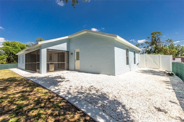 back of property featuring a sunroom, stucco siding, fence, and a gate