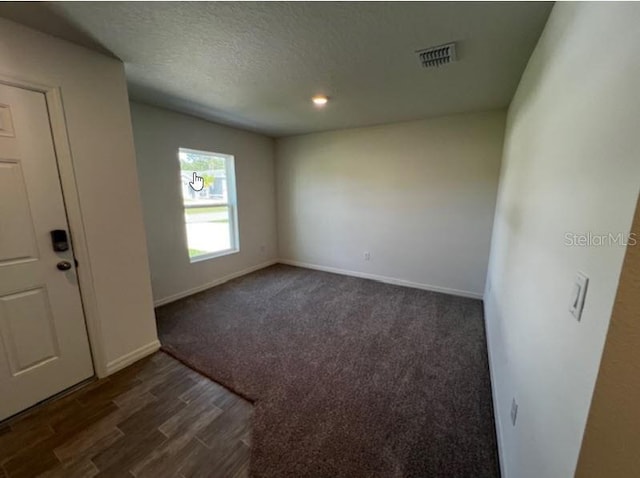 interior space with a textured ceiling, visible vents, baseboards, and dark wood-style flooring