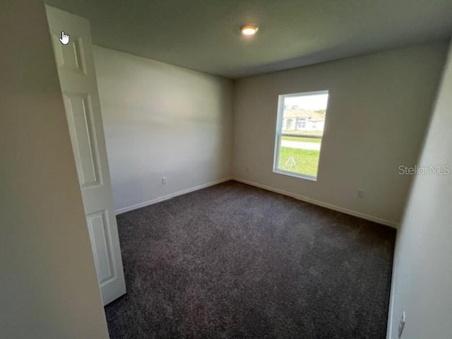 empty room featuring baseboards and dark carpet