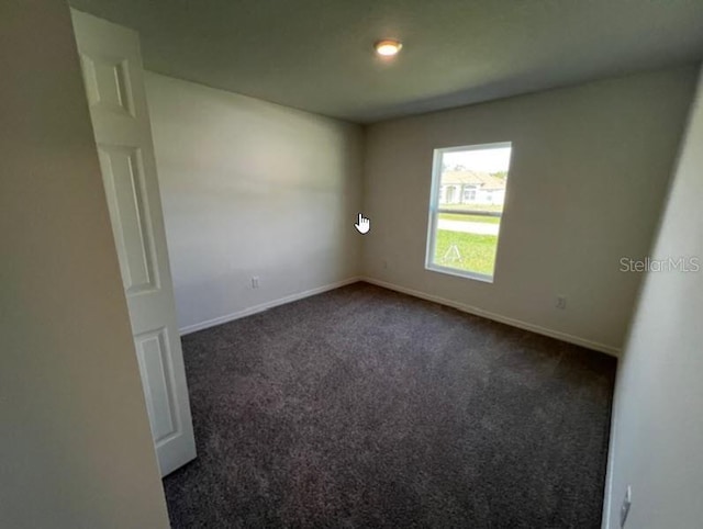 empty room featuring baseboards and dark colored carpet