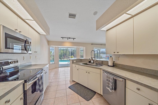 kitchen featuring cream cabinets, stainless steel appliances, a sink, visible vents, and a peninsula