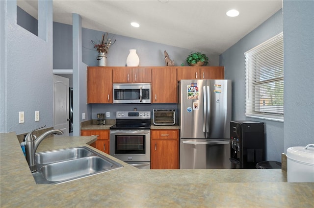 1773 Portage St, North Port, FL 34287 - kitchen featuring appliances with stainless steel finishes, vaulted ceiling, brown cabinets, a sink, and a textured wall