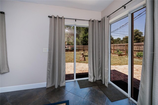 doorway with dark tile patterned flooring and baseboards