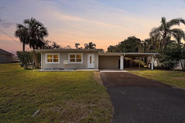 view of front facade featuring stucco siding, aphalt driveway, an attached carport, and a yard