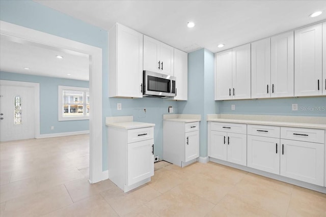 kitchen featuring light countertops, stainless steel microwave, baseboards, white cabinetry, and recessed lighting