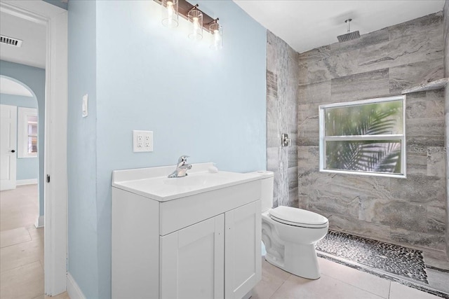 full bath featuring tile patterned floors, toilet, tiled shower, visible vents, and vanity