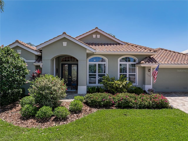mediterranean / spanish home featuring a tile roof, a front yard, stucco siding, french doors, and a garage