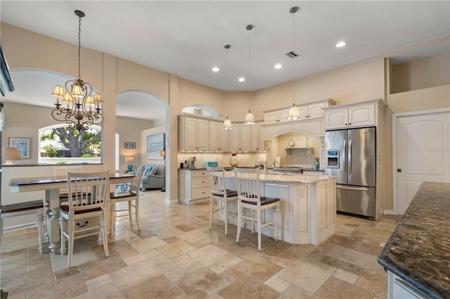 kitchen featuring arched walkways, an inviting chandelier, stone tile flooring, and stainless steel fridge with ice dispenser