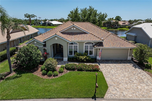 mediterranean / spanish home featuring a tiled roof, a water view, a residential view, a front lawn, and an attached garage