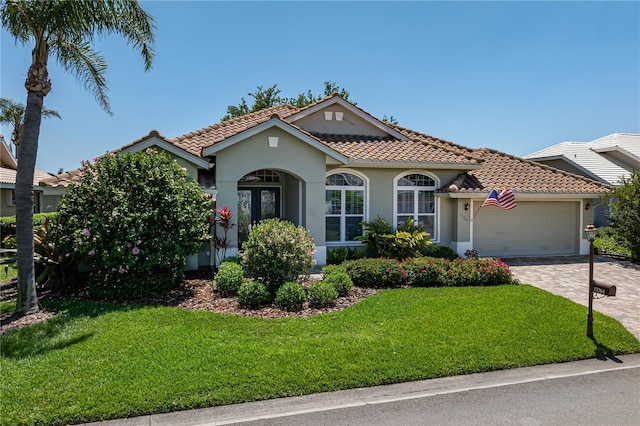 mediterranean / spanish-style house featuring an attached garage, a front lawn, stucco siding, and a tiled roof