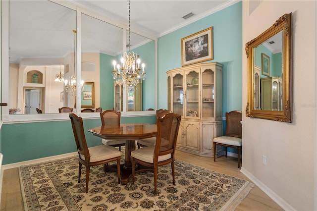 dining space with light wood finished floors, a notable chandelier, visible vents, baseboards, and ornamental molding