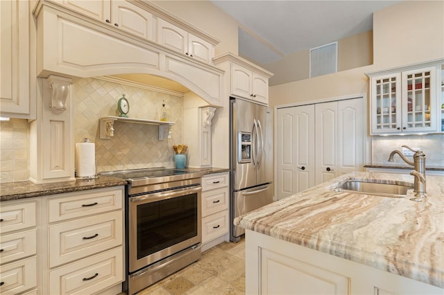 kitchen featuring dark stone countertops, tasteful backsplash, cream cabinets, appliances with stainless steel finishes, and a sink