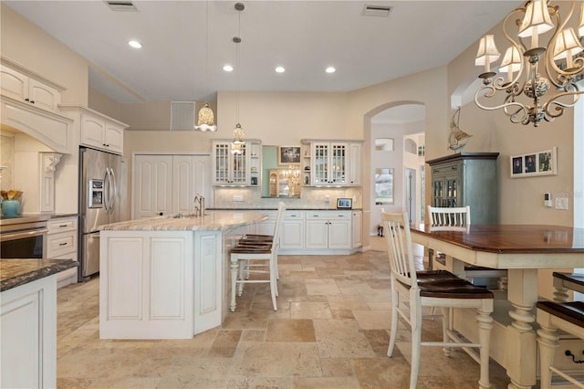 kitchen featuring arched walkways, glass insert cabinets, stone tile flooring, appliances with stainless steel finishes, and visible vents