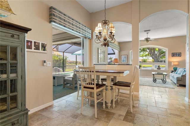 dining space with stone tile flooring, baseboards, a towering ceiling, arched walkways, and ceiling fan with notable chandelier