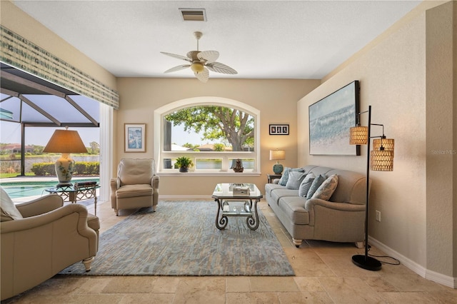living room with a ceiling fan, a wealth of natural light, stone tile flooring, and baseboards