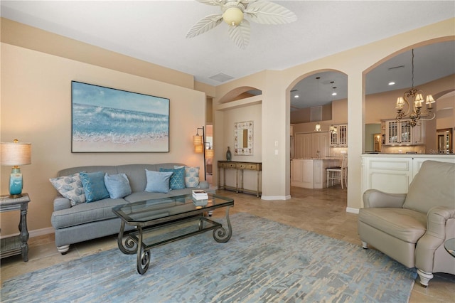 living area with light tile patterned floors, baseboards, arched walkways, and ceiling fan with notable chandelier