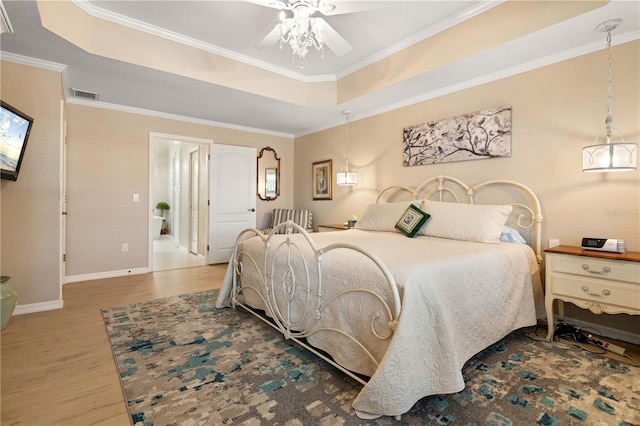 bedroom featuring wood finished floors, ornamental molding, baseboards, visible vents, and a raised ceiling